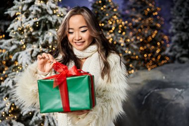 Mutlu genç bir kadın, güzel paketlenmiş bir Noel hediyesini karlı bir arka planda sunar..