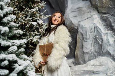 A joyful woman holds a wrapped gift in a snowy winter wonderland. clipart