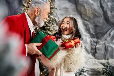 A man and a woman share gleeful moments exchanging colorful gifts during the holiday season. clipart