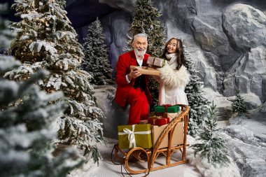 Karlı bir manzarada, Noel Baba ve keyifli bir yoldaş hediye alışverişinde bulunuyor.