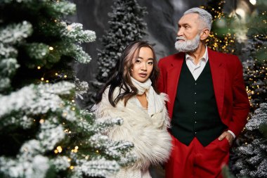 Karla kaplı ağaçlarla çevrili bayram ortamının tadını çıkaran şenlikli bir çift..