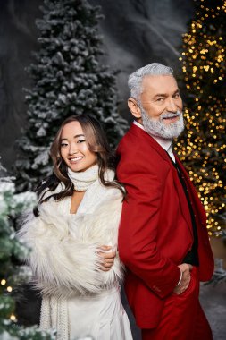 Kırmızı elbiseli, gülümseyen bir adam beyazlı bir kadının yanında duruyor, ikisi de tatil ruhunu kucaklıyor..