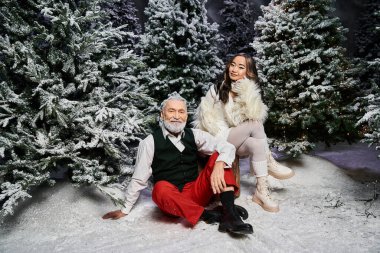 Bir erkek ve bir kadın, karla kaplı ağaçlarla çevrili neşeli bir Noel atmosferinin tadını çıkarıyorlar..