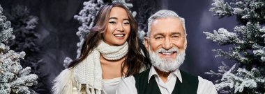 Neşeli genç bir kadın ve gülümseyen yaşlı bir adam Noel boyunca karlı ağaçların arasında kutlama yapıyorlar..