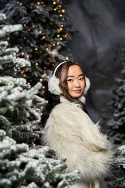 Karla kaplı ağaçların arasında genç bir kadın Noel mevsiminin şenlikli ruhunu kucaklıyor..
