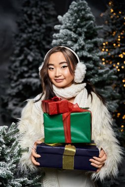 Neşeli bir kadın, karlı kış harikalar diyarında parlak Noel hediyeleriyle poz verir..