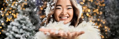 Genç bir insan, pırıl pırıl bir Noel arkaplanı arasında düşen kar tanelerini neşeyle yakalıyor..