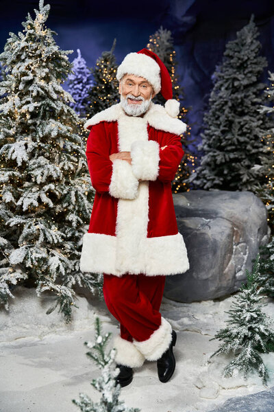 Радостный Санта Клаус позирует в зимней стране чудес в окружении заснеженных деревьев и огней.