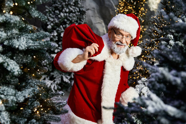 Веселый Санта-Клаус с сумкой, полной подарков прогулки среди снежных рождественских елок.