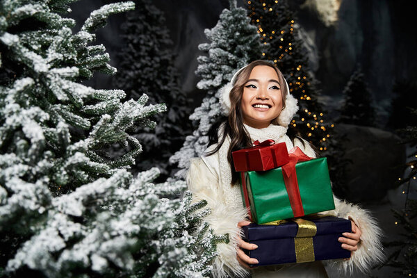 Веселый молодой человек держит красочные обернутые подарки, окруженные морозными деревьями на Рождество.