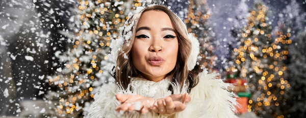A joyful person blows snow into the air amid twinkling holiday decorations during winter.