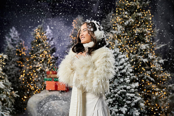Молодая женщина блестяще улыбается, когда снежинки мягко падают вокруг нее, отмечая праздничный сезон.