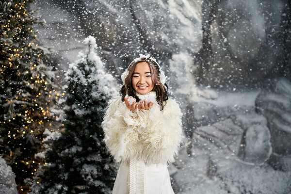 Snowflakes gently fall around a smiling woman dressed in white amid a magical Christmas backdrop.