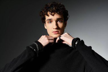 Şık, genç bir adam siyah balıkçı yakasını düzeltirken kıvırcık saçlarını karanlık bir ortamda sergiliyor..