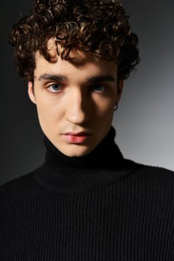 Yakışıklı genç bir adam, kıvırcık saçlı, siyah balıkçı yakalı, kendine güveni ve çekiciliğiyle tarzını sergiliyor..