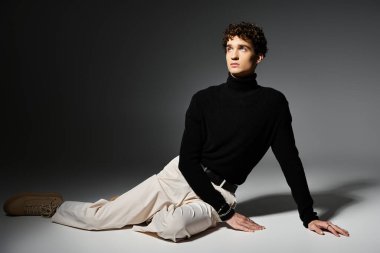 Şık bir genç adam şık bir siyah balıkçı yaka ile şık bir şekilde uzanır, moda anlayışını gösterir..