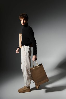 Kıvırcık saçlı yakışıklı genç adam alışveriş torbalarıyla poz veriyor, Kara Cuma 'yı şık bir şekilde kutluyor..