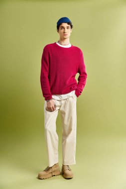 Genç bir adam pembe bir kazakla cazibesini sergiliyor. Canlı, pastel yeşil bir arka plana zarifçe poz veriyor..