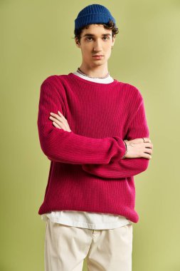 Dressed in a vibrant pink sweater, a young man stands with arms crossed on a pastel green background. clipart