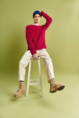 Yakışıklı genç bir adam pembe bir süveter içinde poz veriyor, yeşil renkli bir arka plana karşı rahat bir moda sergiliyor..