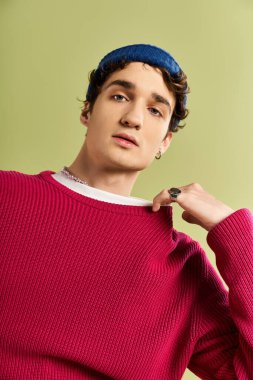 Çekici bir genç adam, yeşil bir duvarın önünde dururken pembe bir kazakla moda anlayışını sergiliyor..