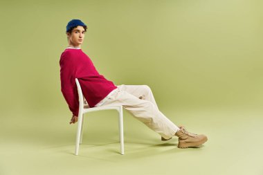 Pembe kazaklı şık bir genç adam yeşil bir arka plana karşı güvenle bir sandalyeye yaslanıyor..