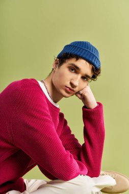 Pembe kazaklı, kendine güvenen genç bir adam, soluk yeşil bir zemine karşı rahat bir poz verir..