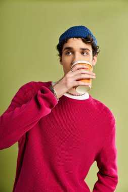 Modaya uygun genç bir adam sıcak bir içecekten hoşlanır. Sıcak, pembe bir süveter ve pastel bir arka planda ışıldayan bir cazibe..