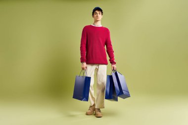 Kıvırcık saçlı şık bir genç adam alışveriş çantalarını heyecanla tutuyor ve Kara Cuma 'yı stüdyoda kutluyor..