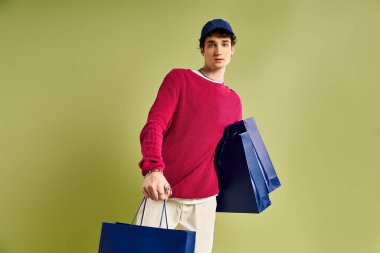 Kıvırcık saçlı şık bir genç adam canlı bir stüdyo ortamında alışveriş çantaları sergiliyor..