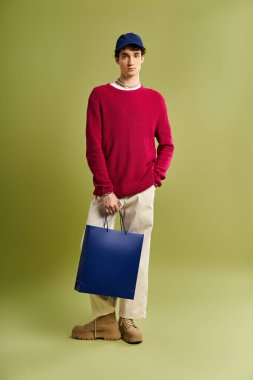 Kıvırcık saçlı modaya uyan genç bir adam stüdyoda renkli çantalar tutarken Kara Cuma alışverişinin tadını çıkarıyor..