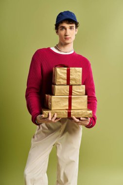 A stylish young man with curly hair proudly presents colorful Christmas gifts in a bright studio setting. clipart