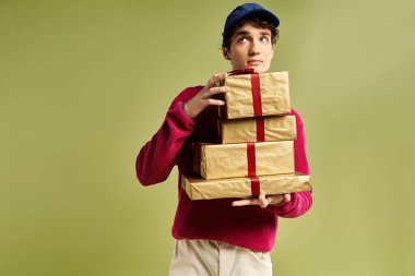 Kıvırcık saçlı genç bir adam güzel paketlenmiş Noel hediyelerini parlak bir stüdyoda tutuyor..