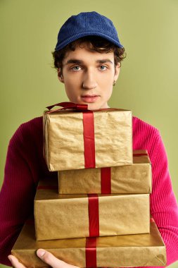 Kıvırcık saçlı şık bir genç adam yeşil bir stüdyoda Noel hediyelerini paketliyor..