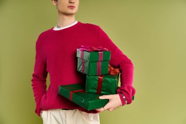 Çekici bir genç adam renkli bir stüdyo ortamında güzel paketlenmiş Noel hediyeleri sergiliyor..