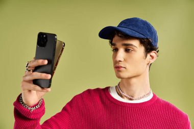 Moda düşkünü genç bir adam elinde telefonuyla canlı pembe bir kazak ve oyuncu aksesuarlar sergiliyor..