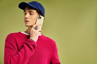 Yakışıklı bir genç, kendine güvenen bir telefonla poz veriyor. Pembe süveter ve şık aksesuarlar sergiliyor..