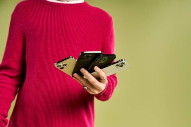 Canlı pembe kazaklı şık bir genç adam, kendine güvenini ve tarzını ifade eden birden fazla akıllı telefon tutuyor..