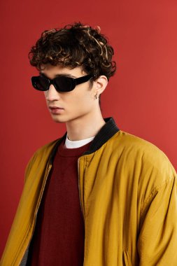 Sarı ceketli ve kıvırcık saçlı çekici genç bir adam kırmızı bir fona karşı güven yayıyor..