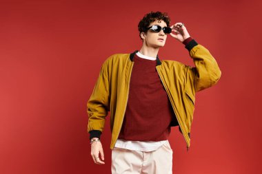 Neşeli bir bakışla, şık bir genç adam sarı ceketini kırmızı arka planda gösterir..