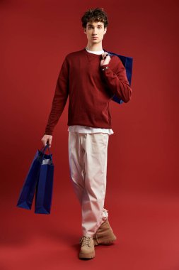 Kıvırcık saçlı yakışıklı genç bir adam Kara Cuma alışverişini sever, şık bulgularını bir stüdyoda sergiler..