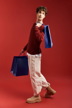 Kıvırcık saçlı şık bir genç adam Kara Cuma 'nın heyecanını kutlarken alışveriş torbaları tutuyor..