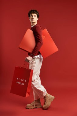 A handsome young man joyfully carries bright shopping bags during Black Friday in a bold studio backdrop. clipart