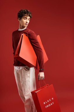 A stylish young man holds festive shopping bags, celebrating his successful Black Friday purchases. clipart