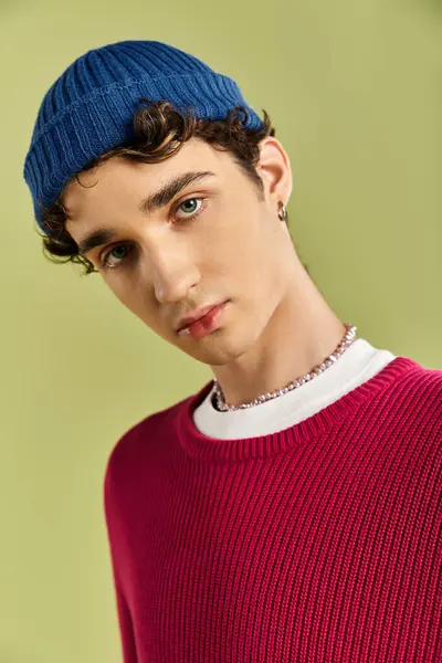 Çekici özellikleri olan genç bir adam kendine güvenen bir poz verirken pembe bir kazak ve mavi bir bere giyer..