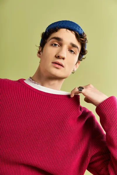 Çekici bir genç adam, yeşil bir duvarın önünde dururken pembe bir kazakla moda anlayışını sergiliyor..