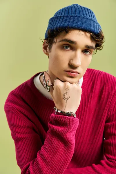 Bu genç adam tarzını pembe kazak ve mavi bereyle sergiliyor, yumuşak yeşil bir arka planla çerçevelenmiş..