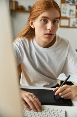 A focused young man sketches digital art on a tablet in a sunlit home workspace. clipart