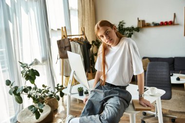 A young man in a white t shirt relaxes on a desk in a cozy and modern room clipart