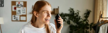 Genç bir adam sıcak bir odada telefonuyla sohbet ederken geniş bir gülümseme sergiliyor..
